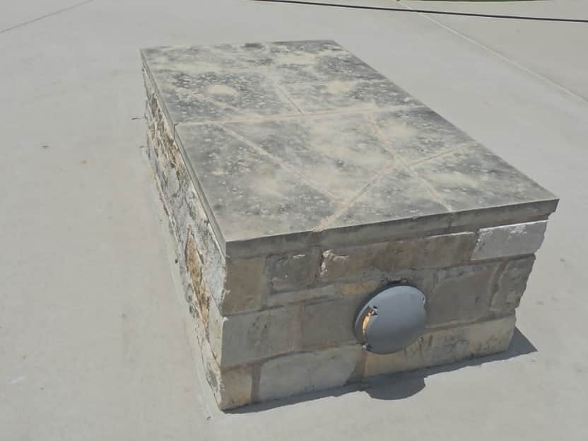 Limestone cap on a stone planter outside an office building, darkened with weathering and organic growth.