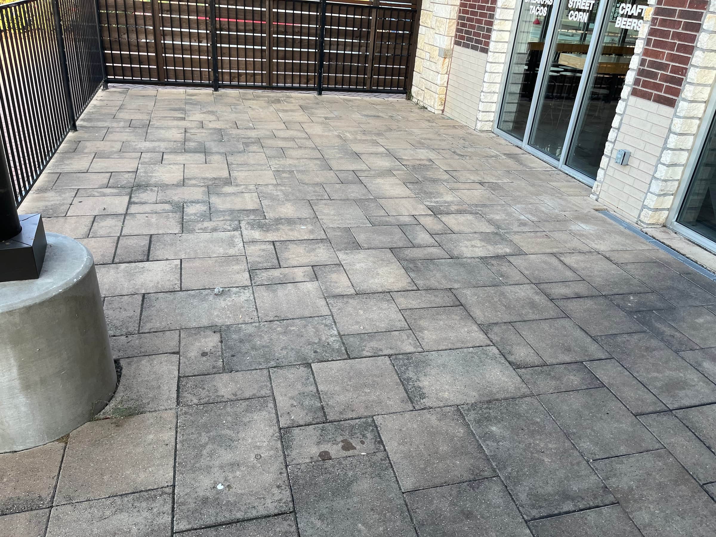 Restaurant patio laid in concrete pavers, uniformly grey with traffic film and weathering before cleaning.